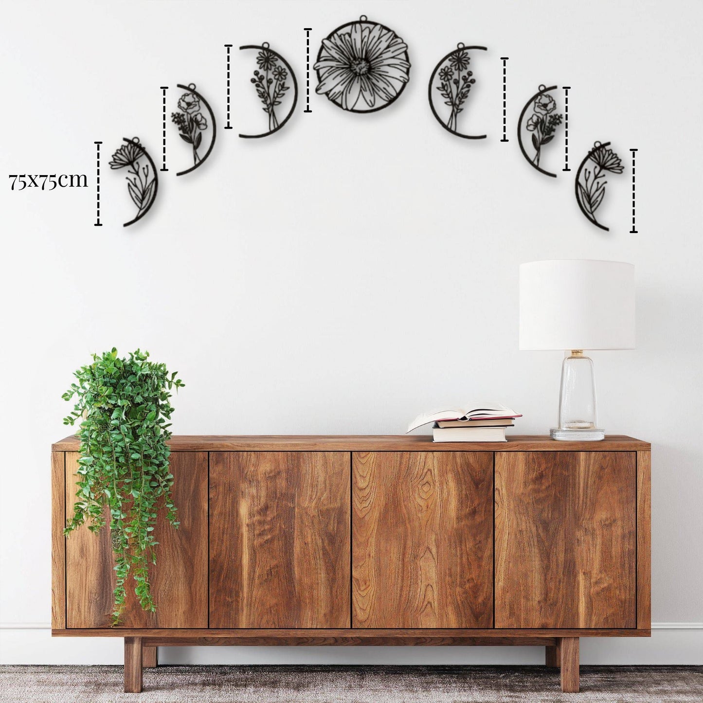 Décoration murale métal lune - ensemble de sculptures murales en métal noir de 75x75cm représentant différentes phases de la lune avec des motifs floraux, accrochées en arc au-dessus d'une console en bois dans un intérieur moderne avec une lampe blanche et une plante verte tombante.